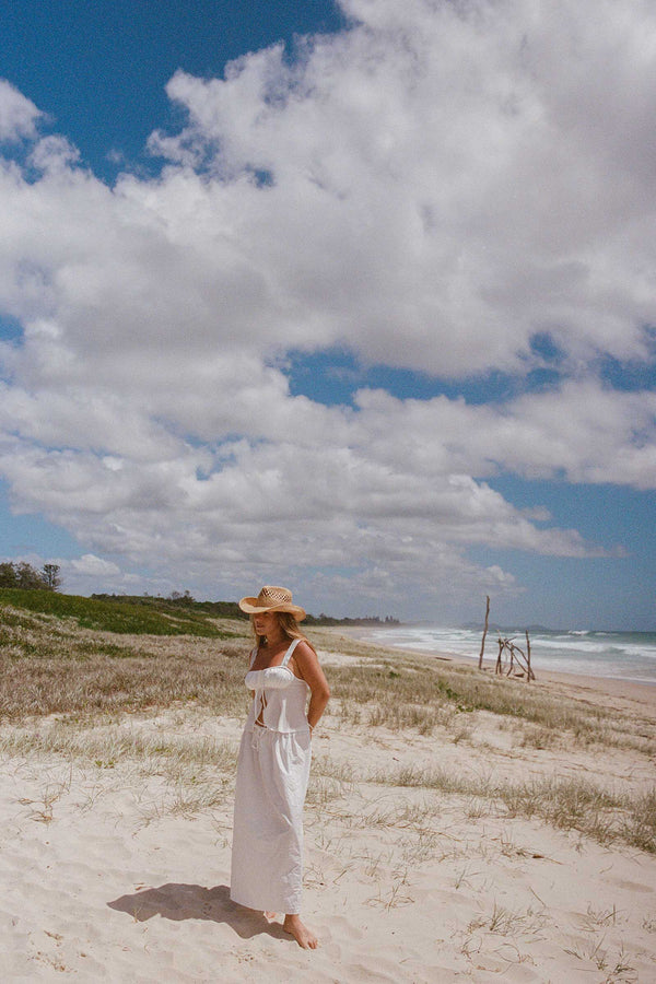 A woman wearing The Desert Cowboy straw fedora hat on a beach with clouds in the sky
