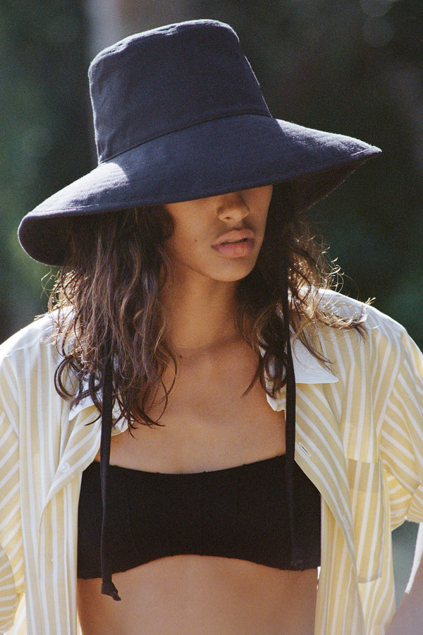 Model wearing a black cotton bucket hat with neck tie, styled with a striped shirt and bikini top