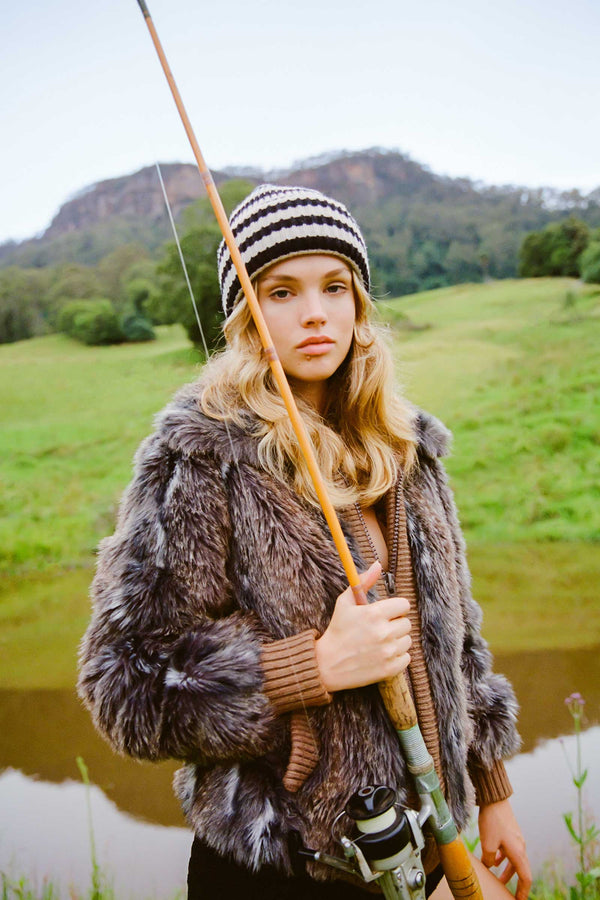 Model wearing Jowan Beanie in Black Stripe, holding a fishing rod by a lake