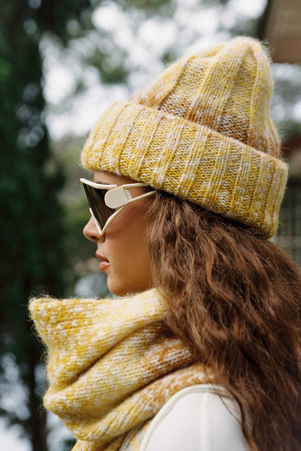 Model wearing a yellow ribbed beanie and matching scarf, showcasing sunset tones.