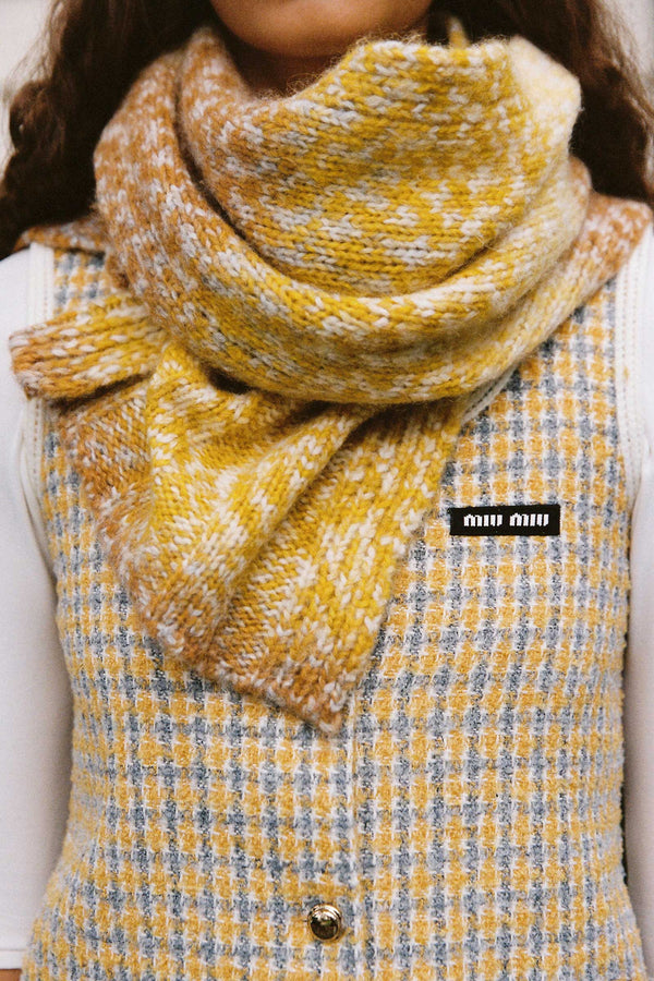 A model wearing a cozy yellow and caramel ribbed scarf made from an alpaca and wool blend.