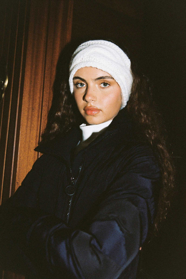 Model wearing a white knitted Lumi headband with a cable pattern