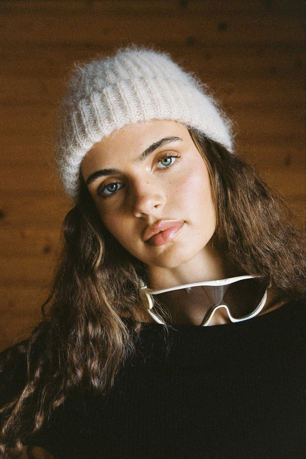 Model wearing a Mason Beanie in Natural color, with sunglasses around her neck.
