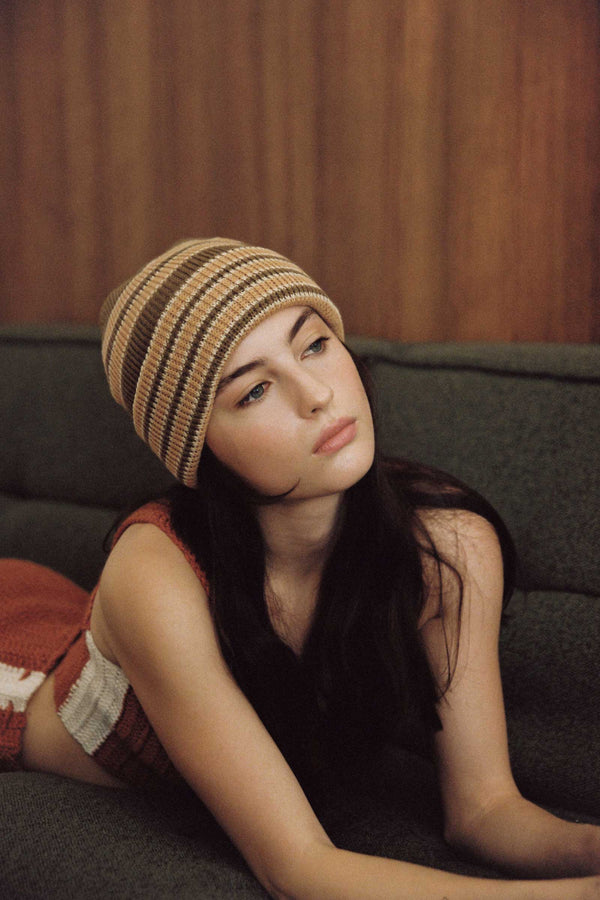 Model wearing a striped brown Momo Beanie, lounging on a green couch.