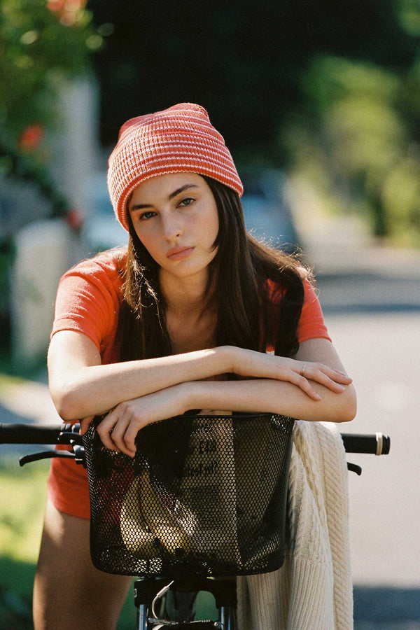 Model wearing Momo Beanie in orange stripes, leaning on a bicycle
