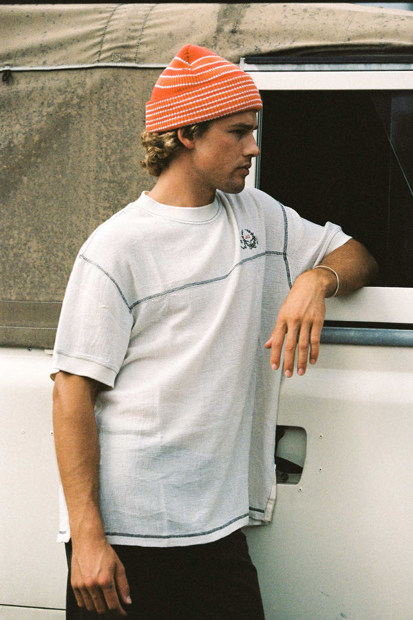 A man wearing an orange striped Momo Beanie, leaning against a vehicle.