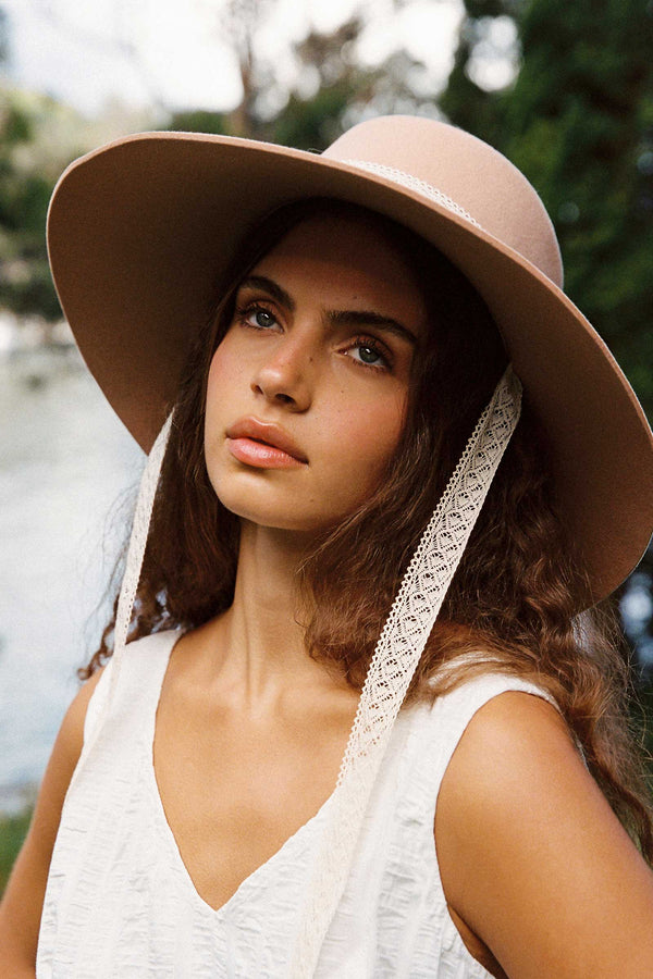 Model wearing the Paloma Midi Wool Felt Boater Hat in Dusty Rose with lace ties, outdoors.