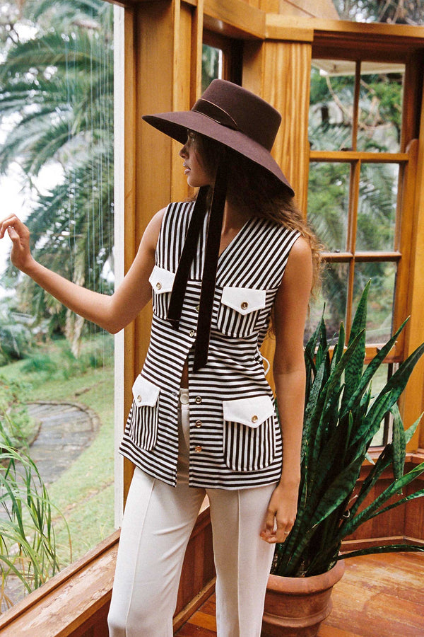 Model wearing the Paloma Midi Wool Felt Boater Hat in Brown, with a striped vest and a natural background.