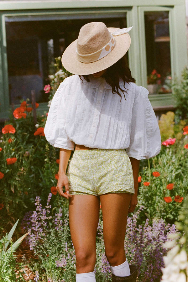 Model wearing a pistachio scarf and hat in a garden with flowers