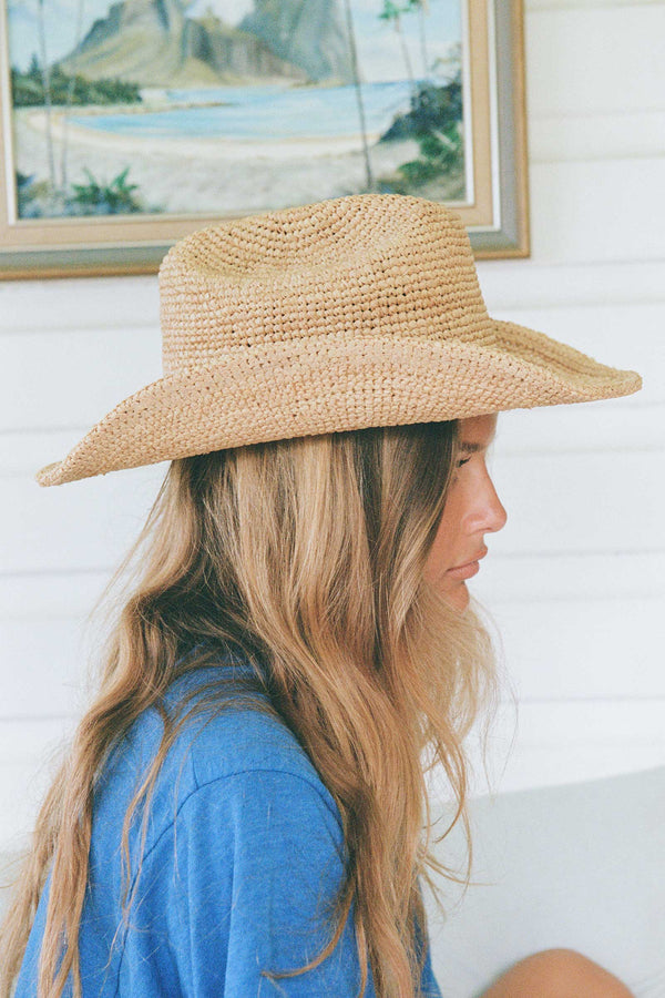 Profile view of a woman wearing a natural raffia cowboy hat, showcasing its texture and style.