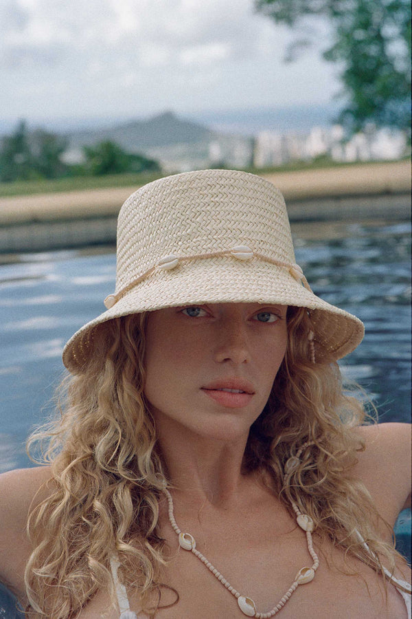 A woman wearing The Inca Bucket straw hat with seashells by a pool