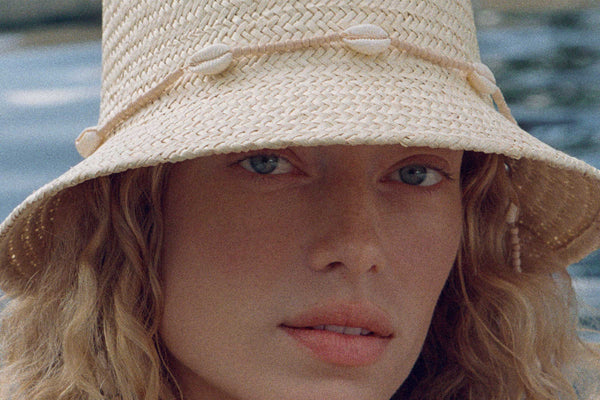 Close-up of a model wearing The Inca Bucket straw hat with seashell chin strap