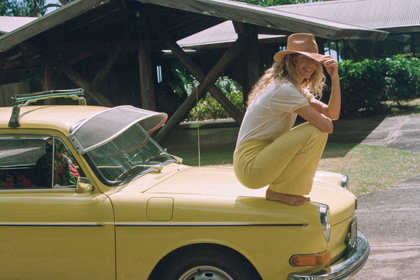Model wearing The Inca Fedora while sitting on a yellow car in a tropical setting