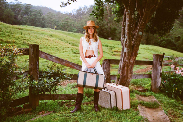 Model wearing The Inca Fedora in a natural setting with suitcases