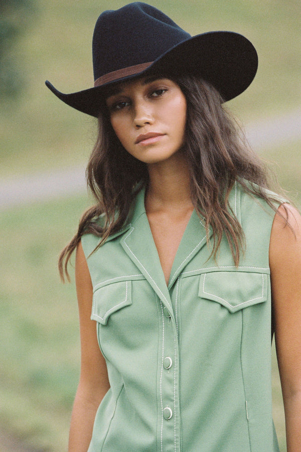 Model wearing a black Wilder Cowboy wool felt hat with a green outfit in an outdoor setting.