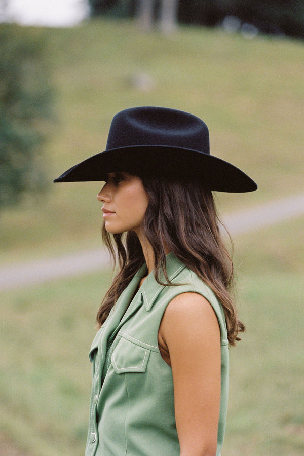 Profile view of a woman wearing a black wool felt cowboy hat, showcasing its wide brim and structured crown.