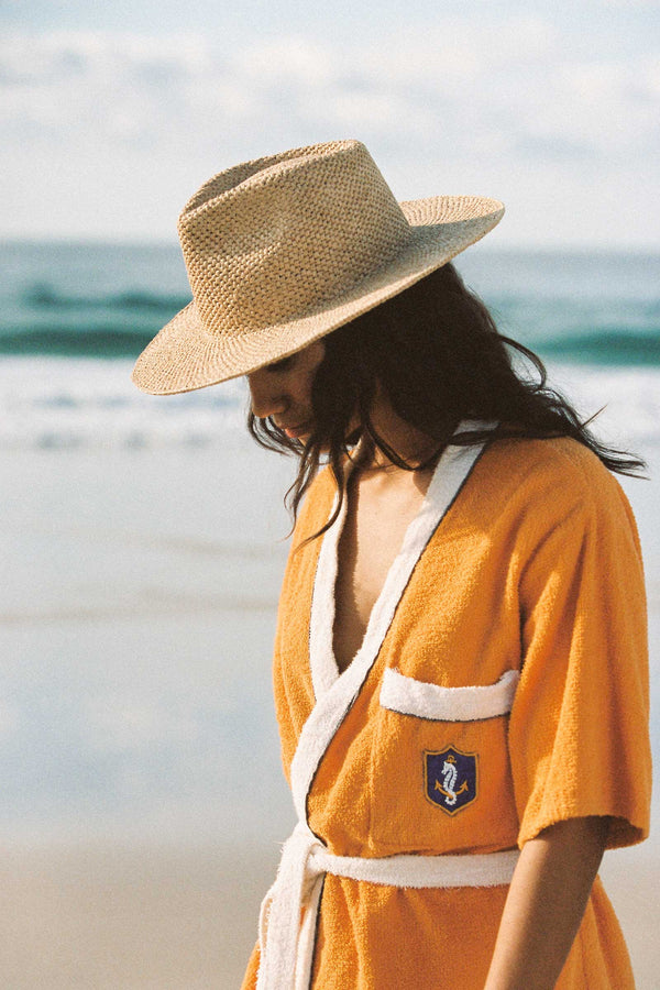 Model wearing the Inca Fedora on the beach, dressed in an orange robe