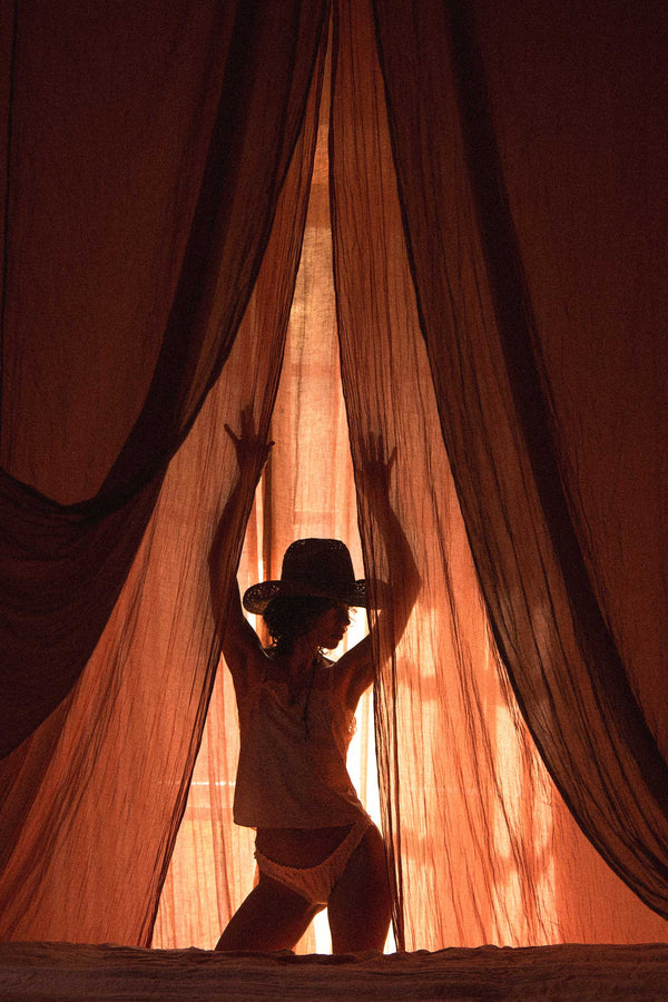 Silhouette of a person wearing a straw cowboy hat behind sheer curtains
