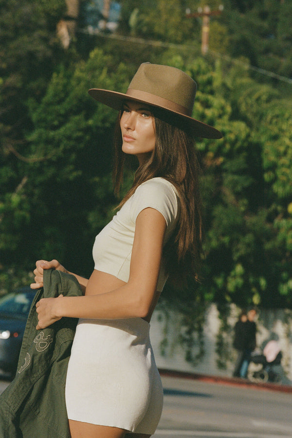 Model wearing a Teak Rancher wool felt fedora hat in brown, outdoors.