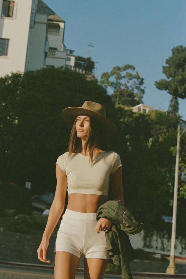 A model wearing a Teak Rancher wool felt fedora hat in a sunny outdoor setting.