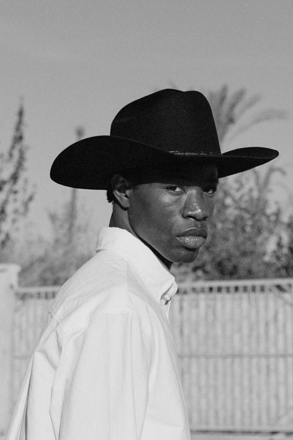 A model wearing The Ridge wool felt cowboy hat in black against a blurred outdoor background.
