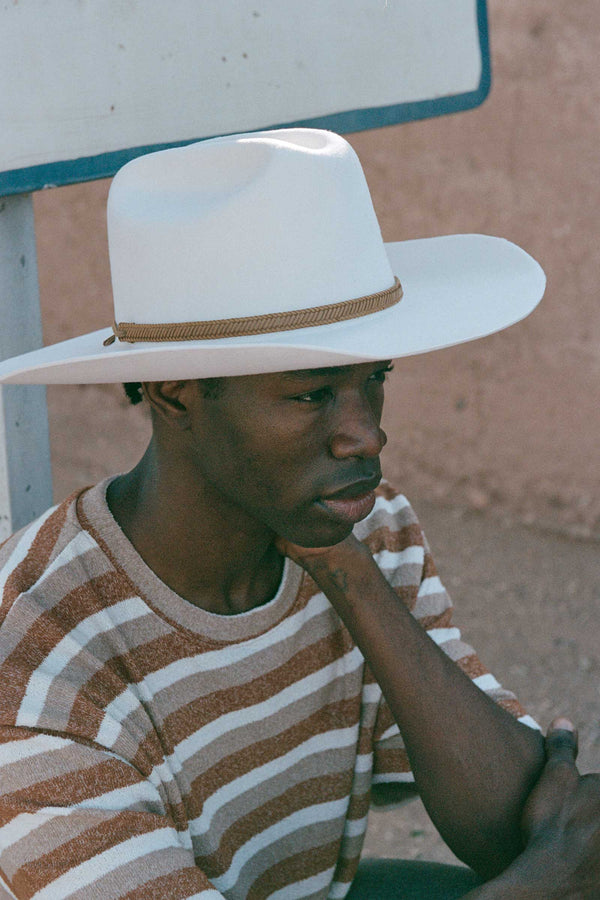 A model wearing The Ridge wool felt cowboy hat in white, featuring a tan band.