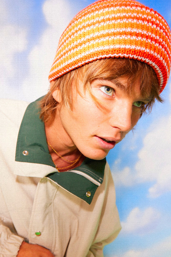 Model wearing an orange striped Momo Beanie against a blue sky background