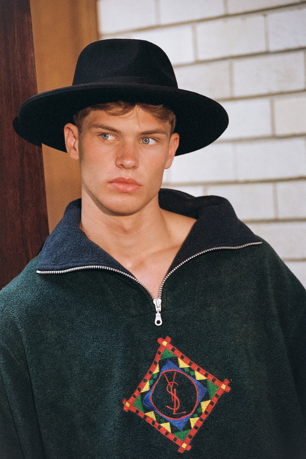 Model wearing a black wool felt fedora hat with a green zip-up fleece top