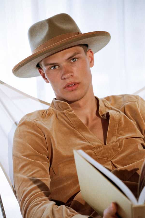 Model wearing Pierre Teak wool felt fedora hat, seated and reading a book.