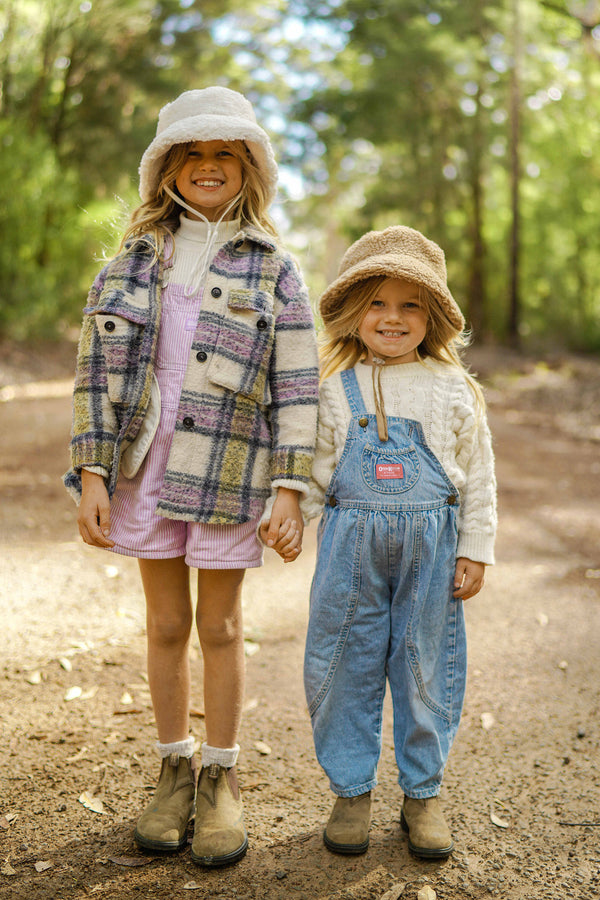 Two children wearing Teddy Bucket hats in a forest setting, one in brown and one in beige.