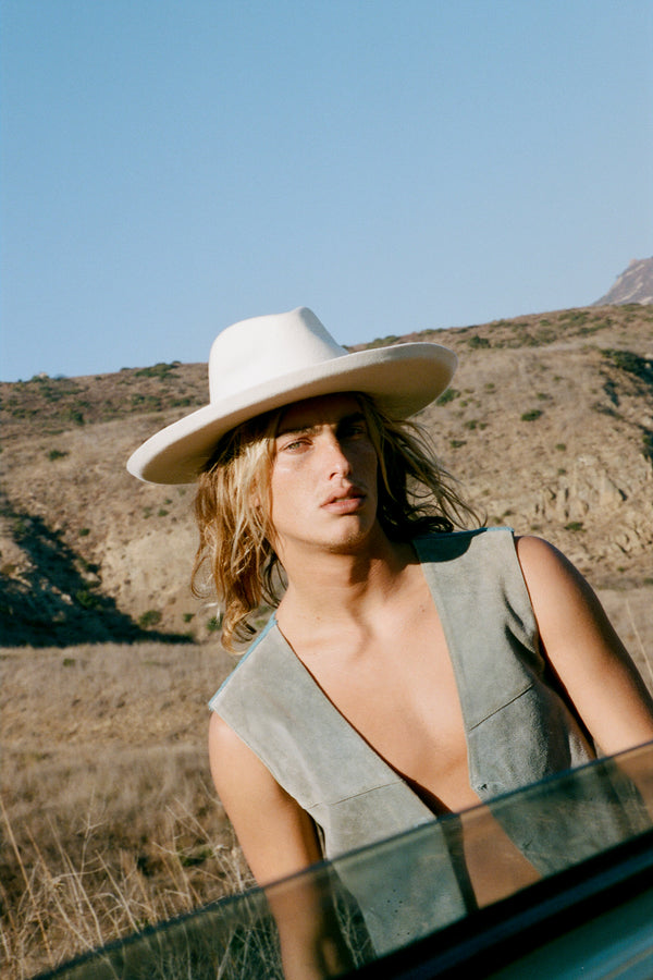 A model wearing The Melodic Fedora in a natural landscape setting.