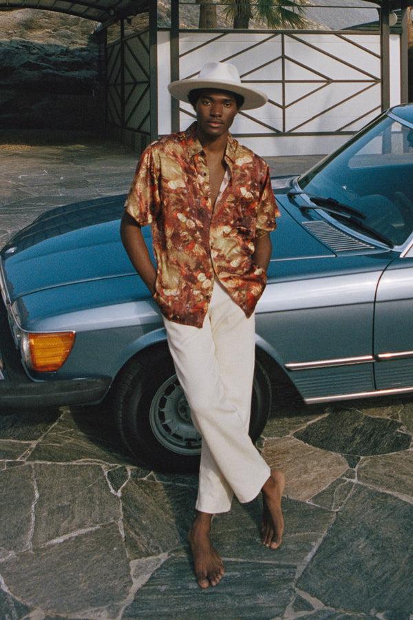 A model wearing The Melodic Fedora in a floral shirt, standing next to a vintage car.