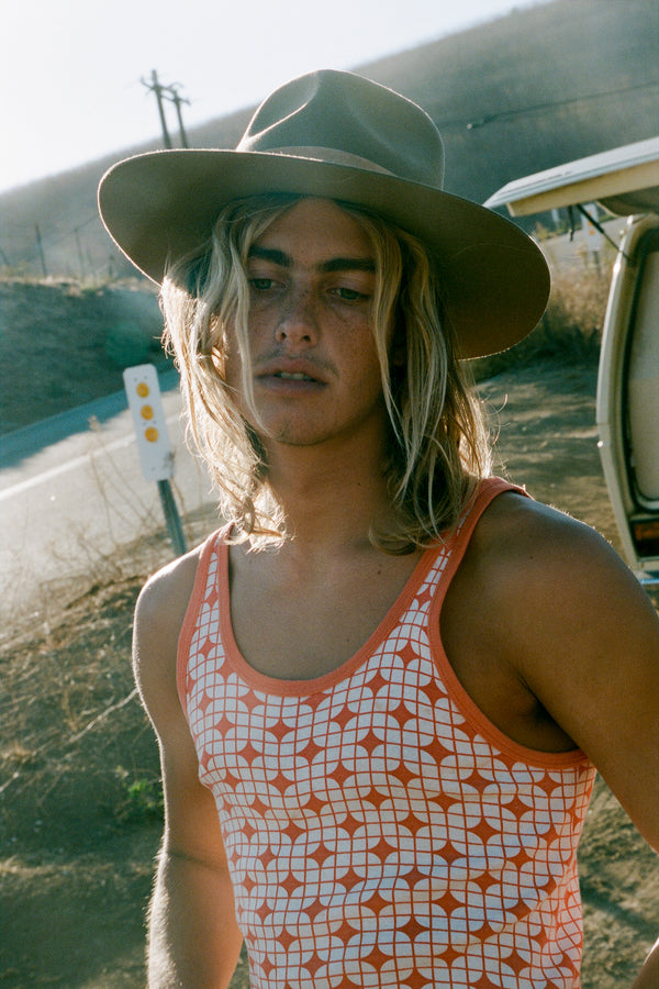 A young man wearing The Mirage wool felt fedora hat in brown, standing outdoors.