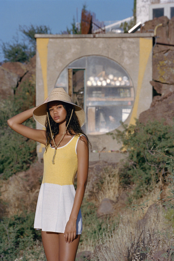 Model wearing The Vista straw cowboy hat in natural color, standing outdoors with a rustic building in the background.