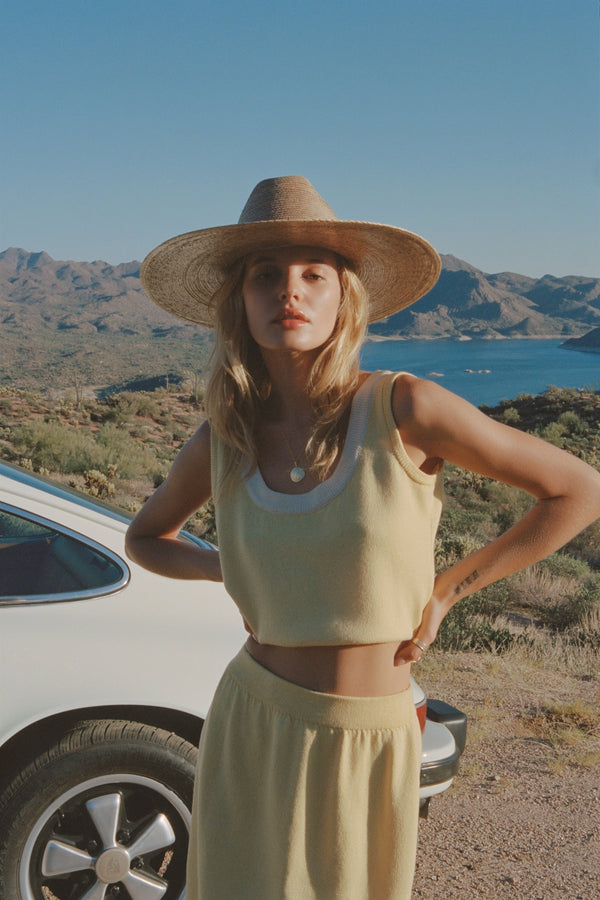 Model wearing a Western Wide Palma straw cowboy hat, standing outdoors with mountains and a lake in the background.