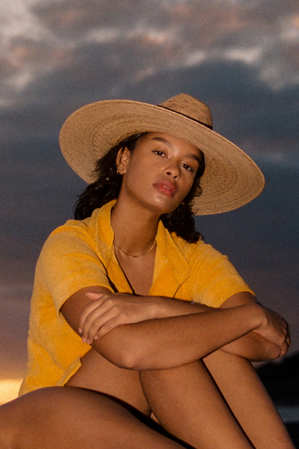 Model wearing a Western Wide Palma straw cowboy hat, sitting outdoors at sunset.
