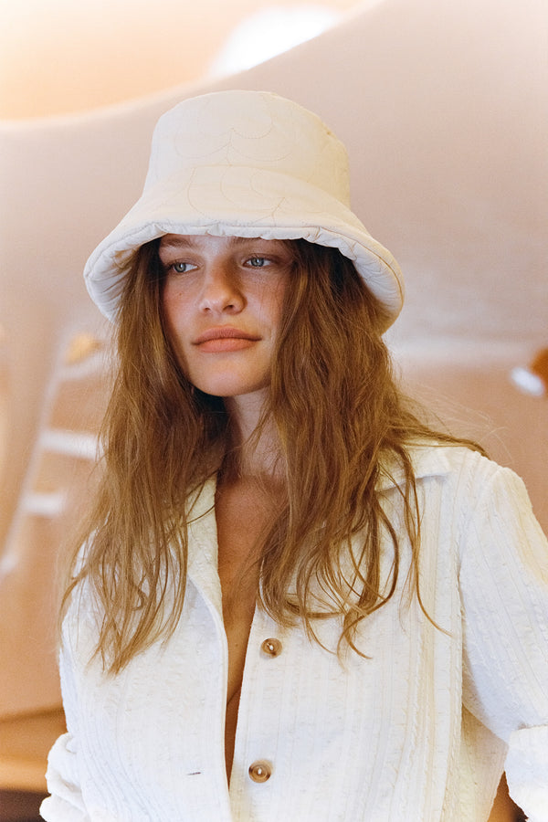 Model wearing a cream puffer bucket hat with custom heart pattern detail.