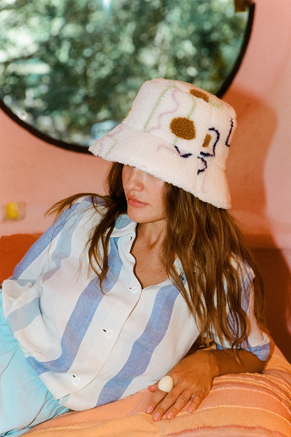 A woman wearing a multicolor Teddy Bucket hat, lounging on a couch.