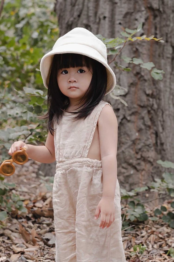 Child wearing a beige cotton bucket hat, holding sunglasses in a natural setting.