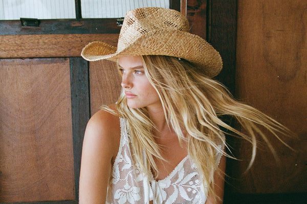 A woman with long hair wearing a straw hat, sitting indoors.