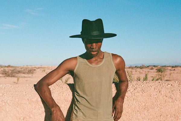 A person wearing a black hat and tank top in a desert landscape