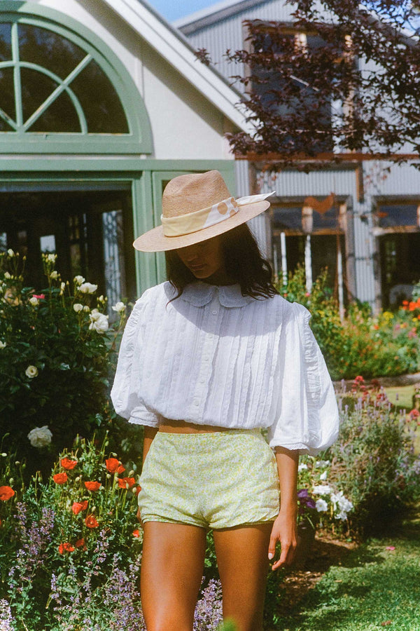 Model wearing a straw hat and white blouse in a garden setting