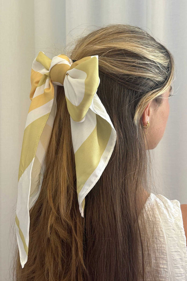 Woman with long hair wearing a yellow and white patterned scarf tied in a bow at the back of her head