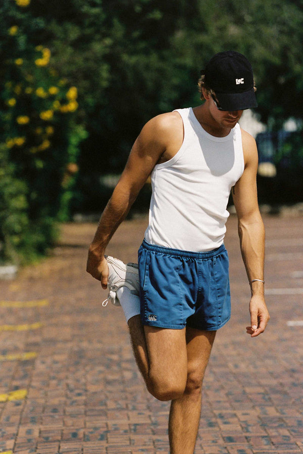 A man wearing a black LOC cap, stretching on a sunny street.