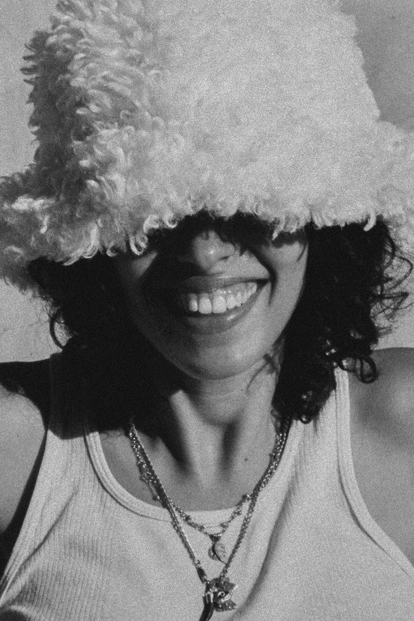 Model wearing a fluffy white bucket hat, smiling, with curly hair